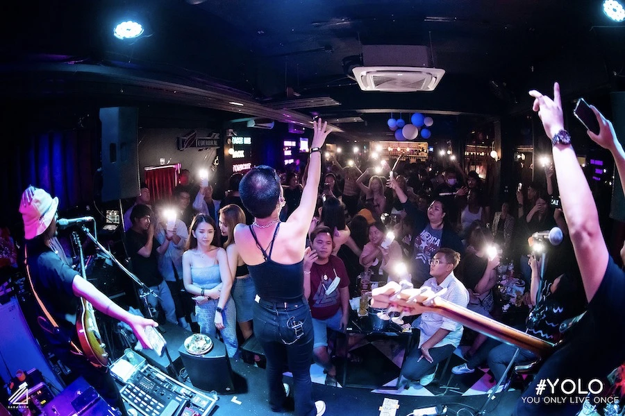 singer singing during a live music event at yolo bangkok bar in front of a room packed with patrons