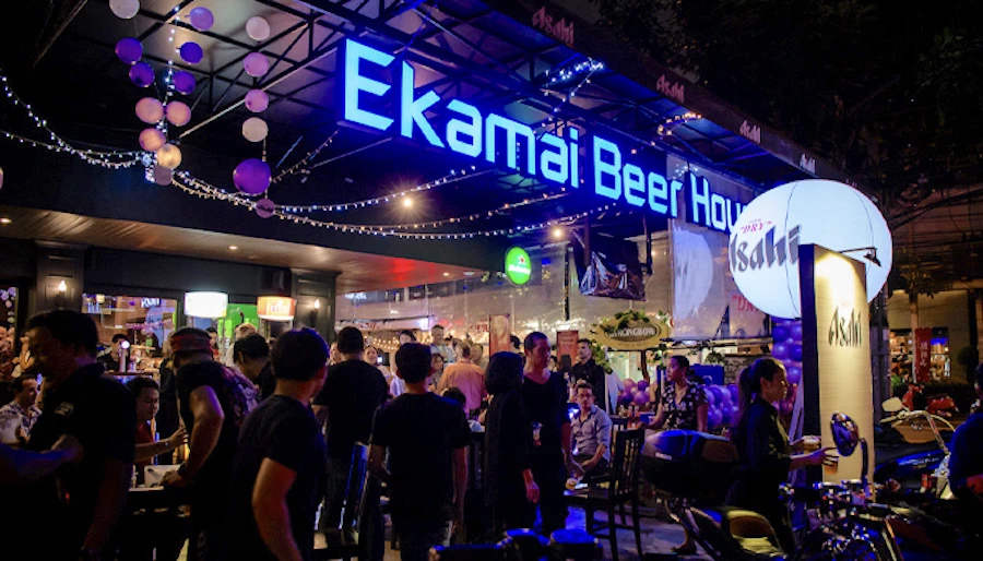 front of ekamai beer house with a large blue sign and a dense crowd of customers