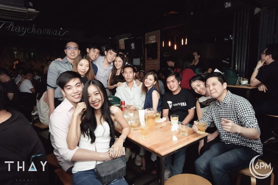 a large group of friends sitting and chilling on a table at thay ekkamai bar drinking thai beer