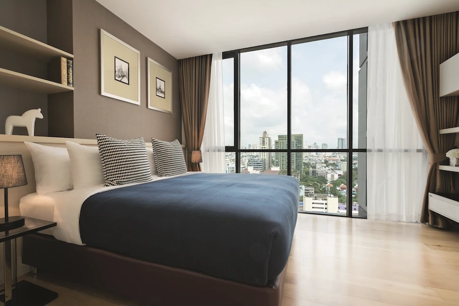 a room in movenpick ekkamai hotel displaying a large comfortable bed a minimalist decoration and a beautiful view of the city of bangkok