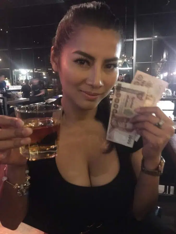Thai bar girl holding a whisky shot and money