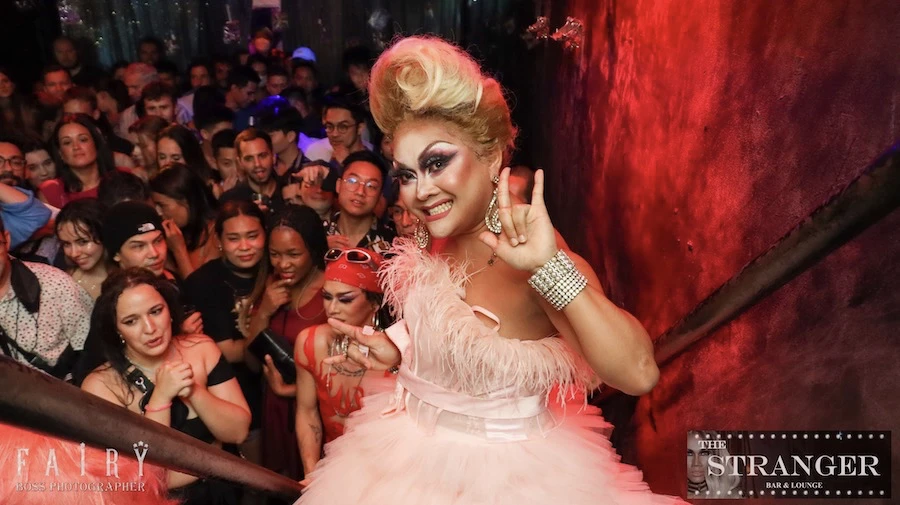 a drag queen is posing and doing a selfie with a crowd at stranger bar in bangkok